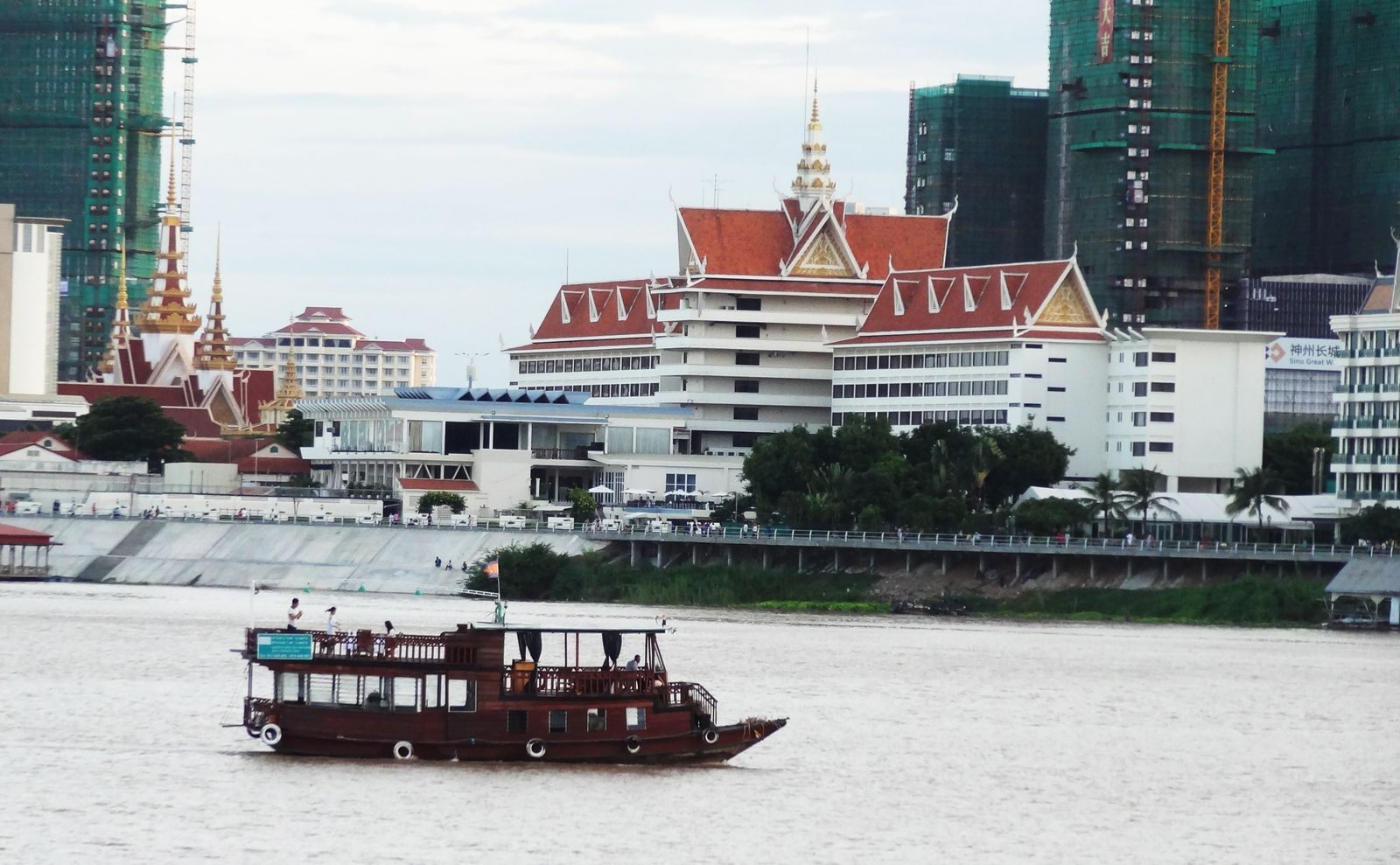 Wooden riverboat cruising past the Royal Palace and Phnom Penh skyline, a classic sight on Southeast Asia river cruises