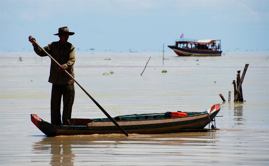 Cambodian fisherman standing in a long wooden boat on the Mekong in Kampong Cham Province