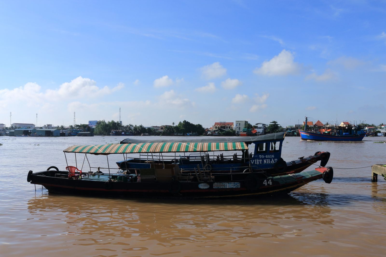 Covered wooden passenger boat on the brown Mekong River in Vietnam under a blue sky